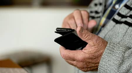 Zdjęcie rąk starszej osoby trzymającej smartfona.