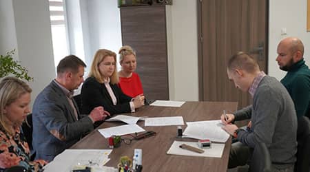 Zdjęcie pięciu osób siedzących przy stole podczas podpisywania dokumentów.